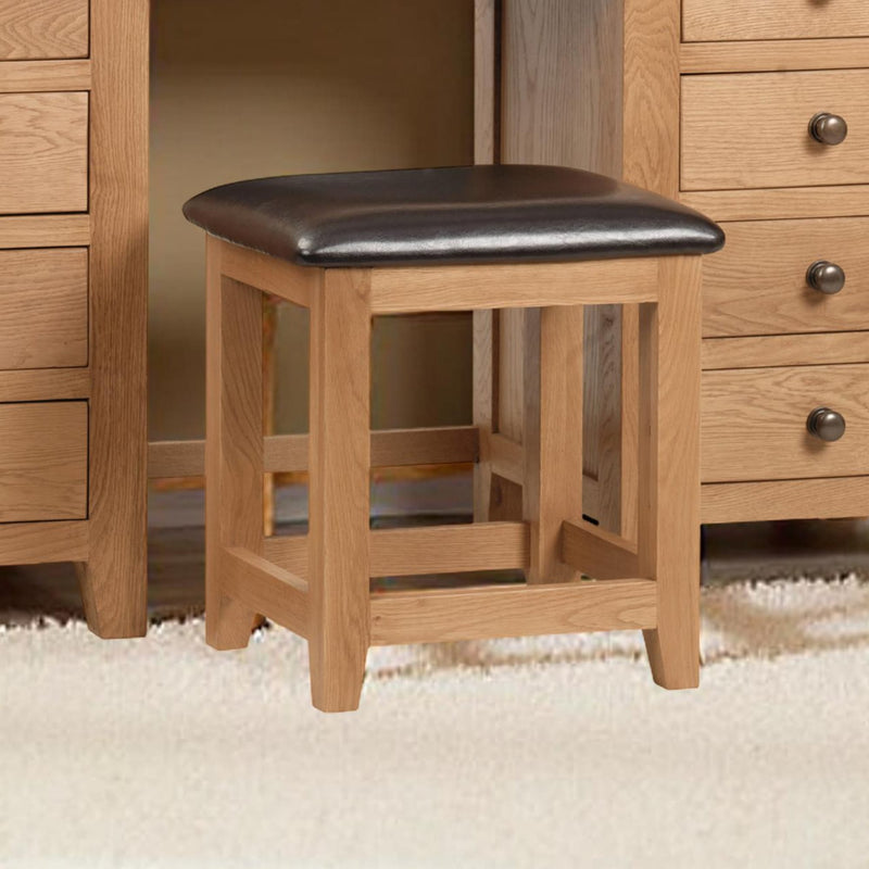 Wooden stool with a black leather seat in front of wooden furniture.
