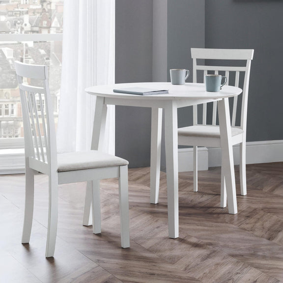 White dining table with chairs in a room with a gray wall and wooden floor.
