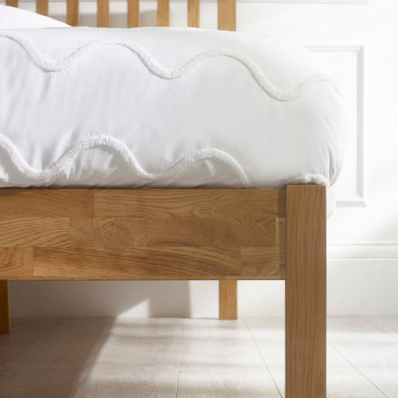 Wooden bed frame with a white mattress on a light wooden floor.