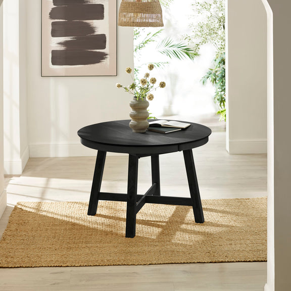Round black table with a vase of flowers in a room with white walls and a rug.