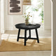 Round black table with a vase of flowers in a room with white walls and a rug.