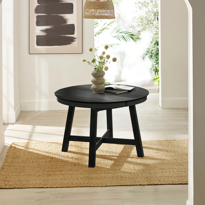 Round black table with a vase of flowers in a room with white walls and a rug.