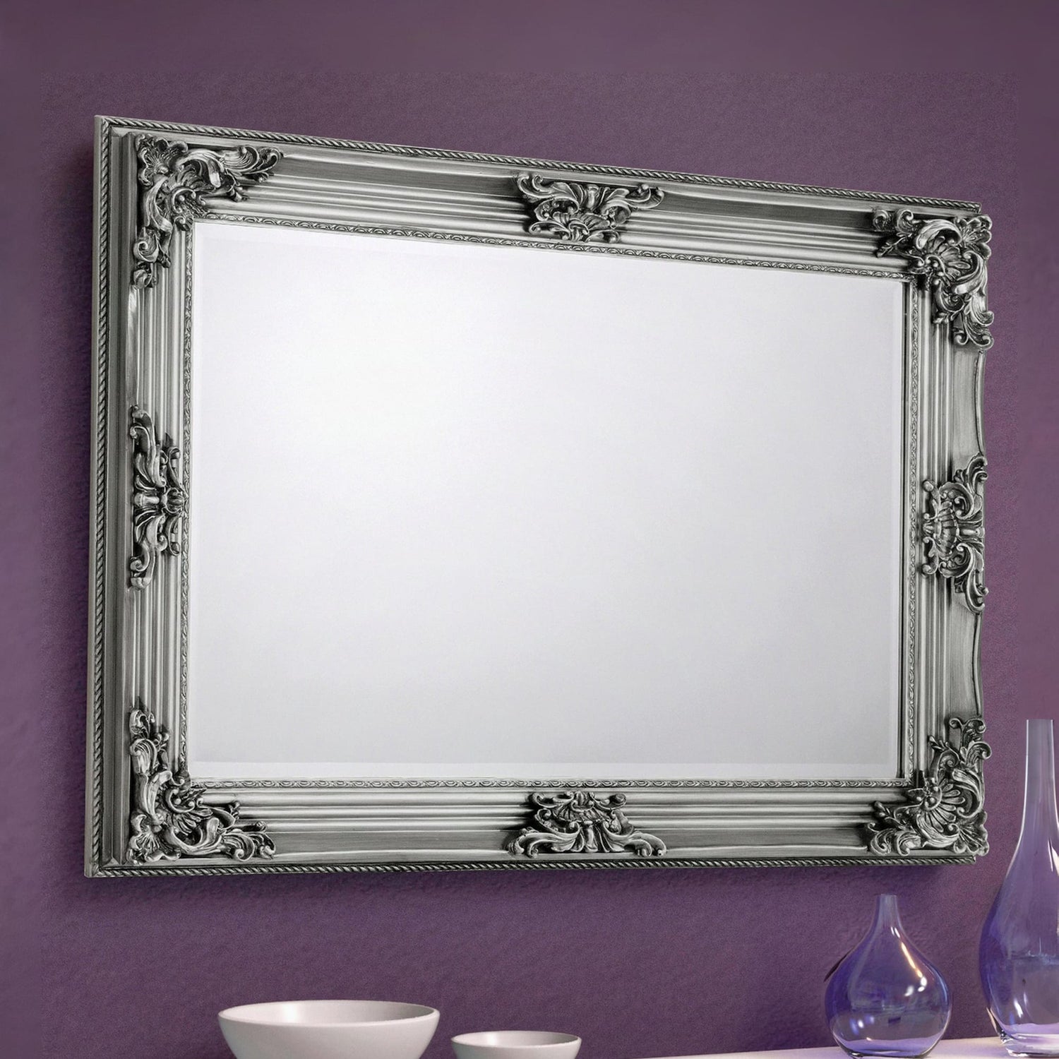 Decorative silver mirror with intricate designs on a purple wall.