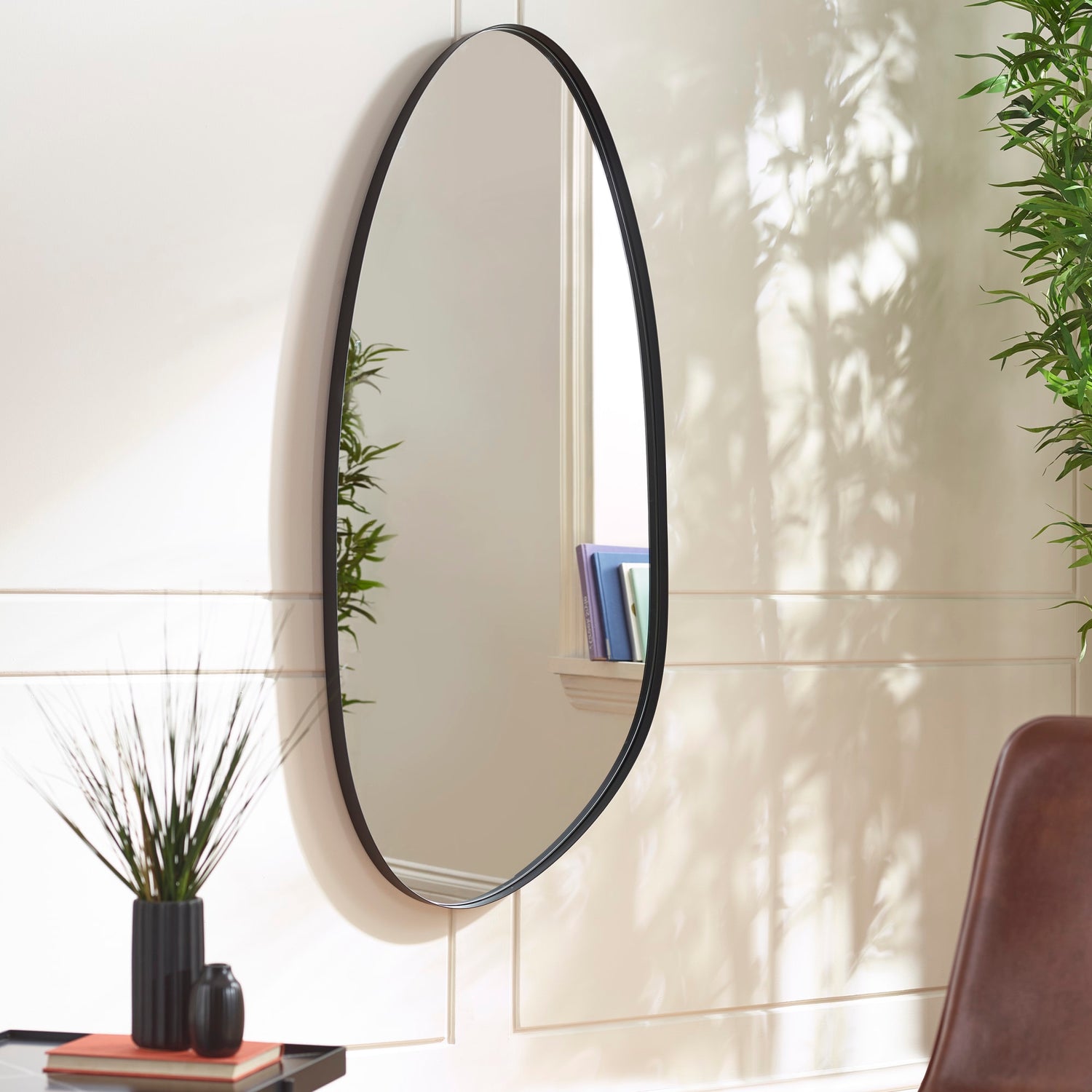 Round mirror with black frame on a wall with plants and books.
