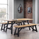 Wooden dining table with benches in a modern room with a brick wall and large window.