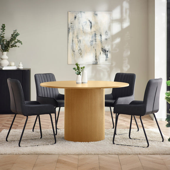 Dining room with a round wooden table and black chairs, featuring a abstract painting on the wall.