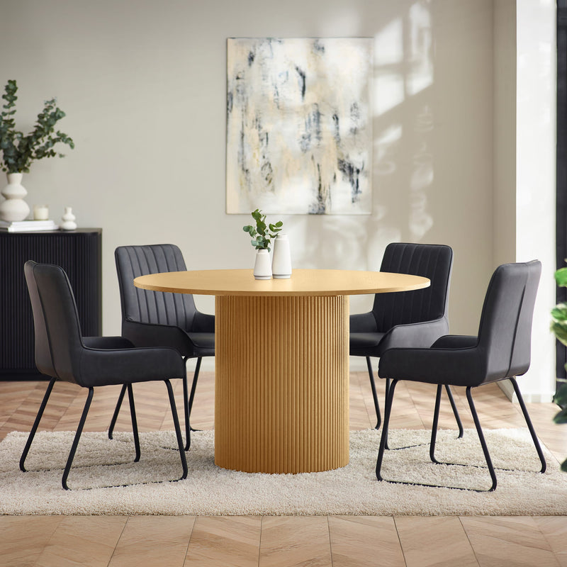 Dining room with a round wooden table and black chairs, featuring a abstract painting on the wall.