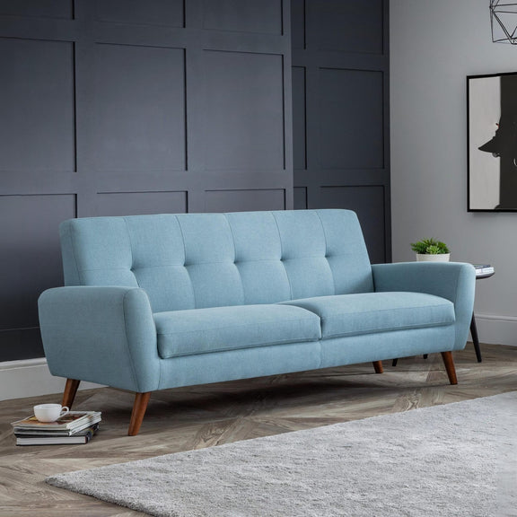 Blue sofa in a room with a dark paneled wall and a gray rug.