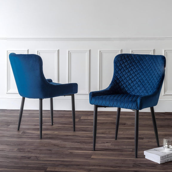 Two blue chairs on a wooden floor with a white paneled wall in the background.