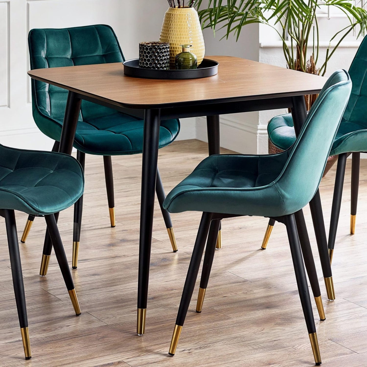 Dining table set with teal chairs and gold legs in a room with plants.