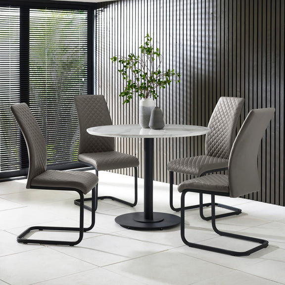 Modern dining set with four gray chairs and a round table in a room with large windows.