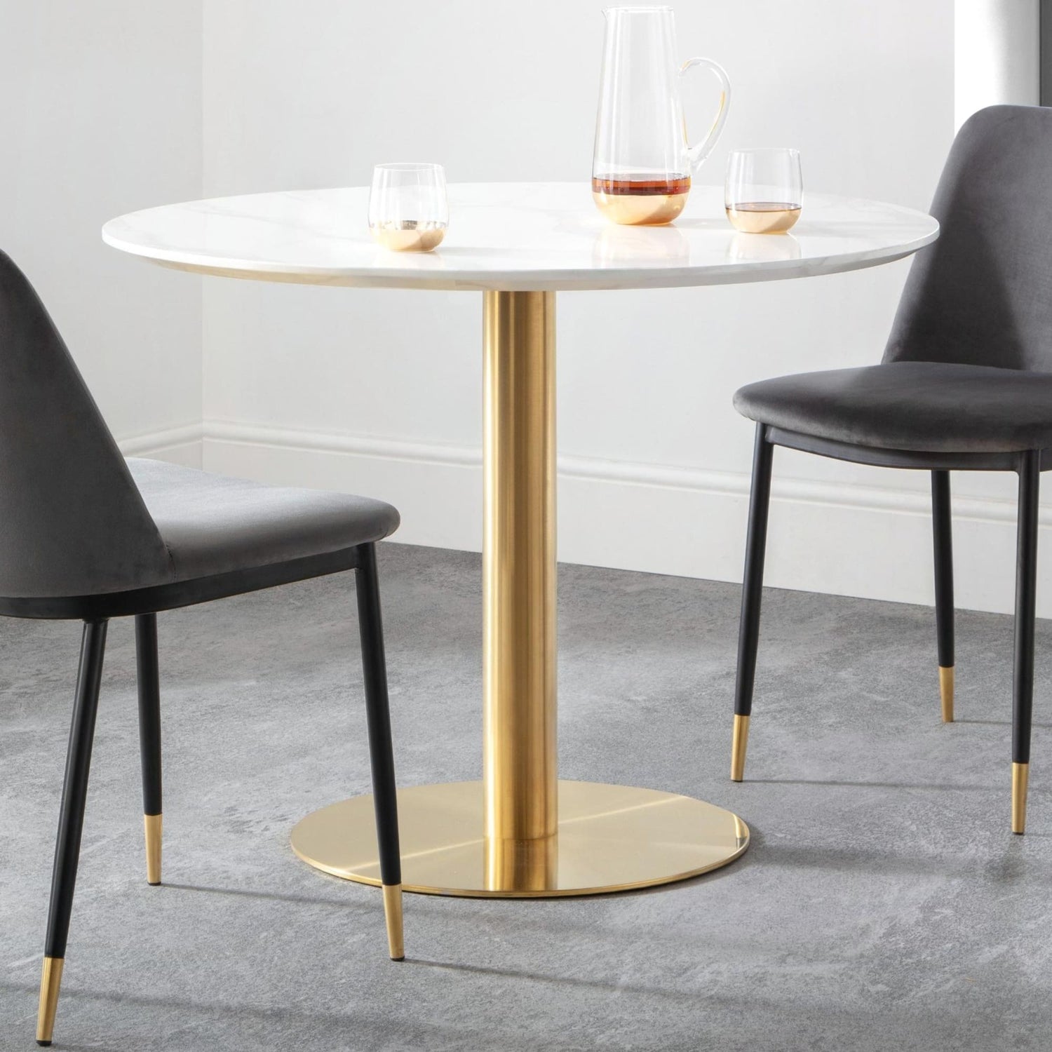 Round dining table with gold base and two gray chairs in a modern setting