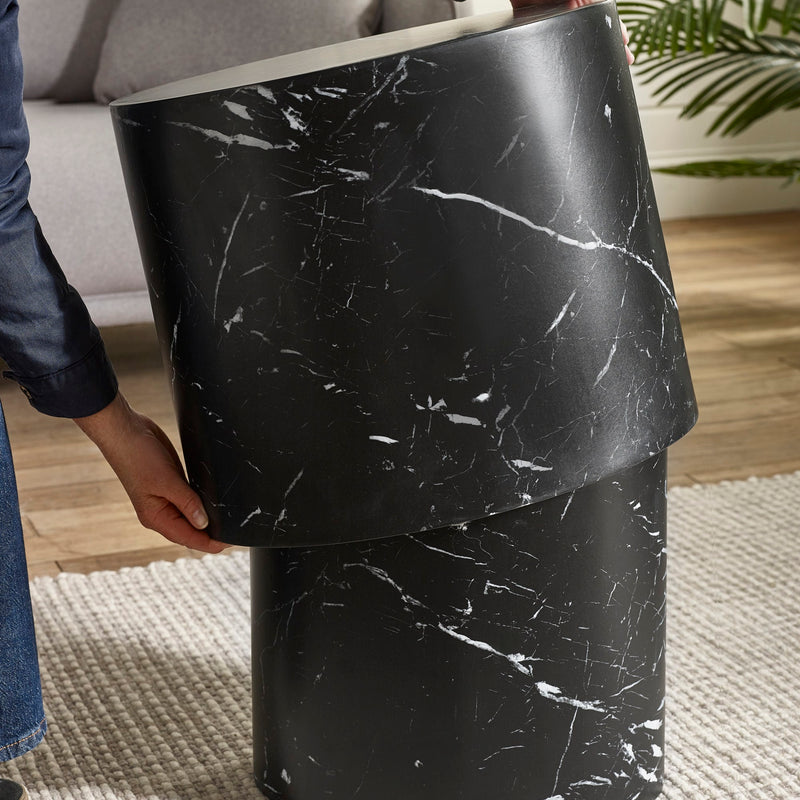 Person holding a black marble-patterned cylindrical object indoors.