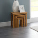 Set of three wooden nesting tables with a decorative vase and photo frame on a gray wall background.