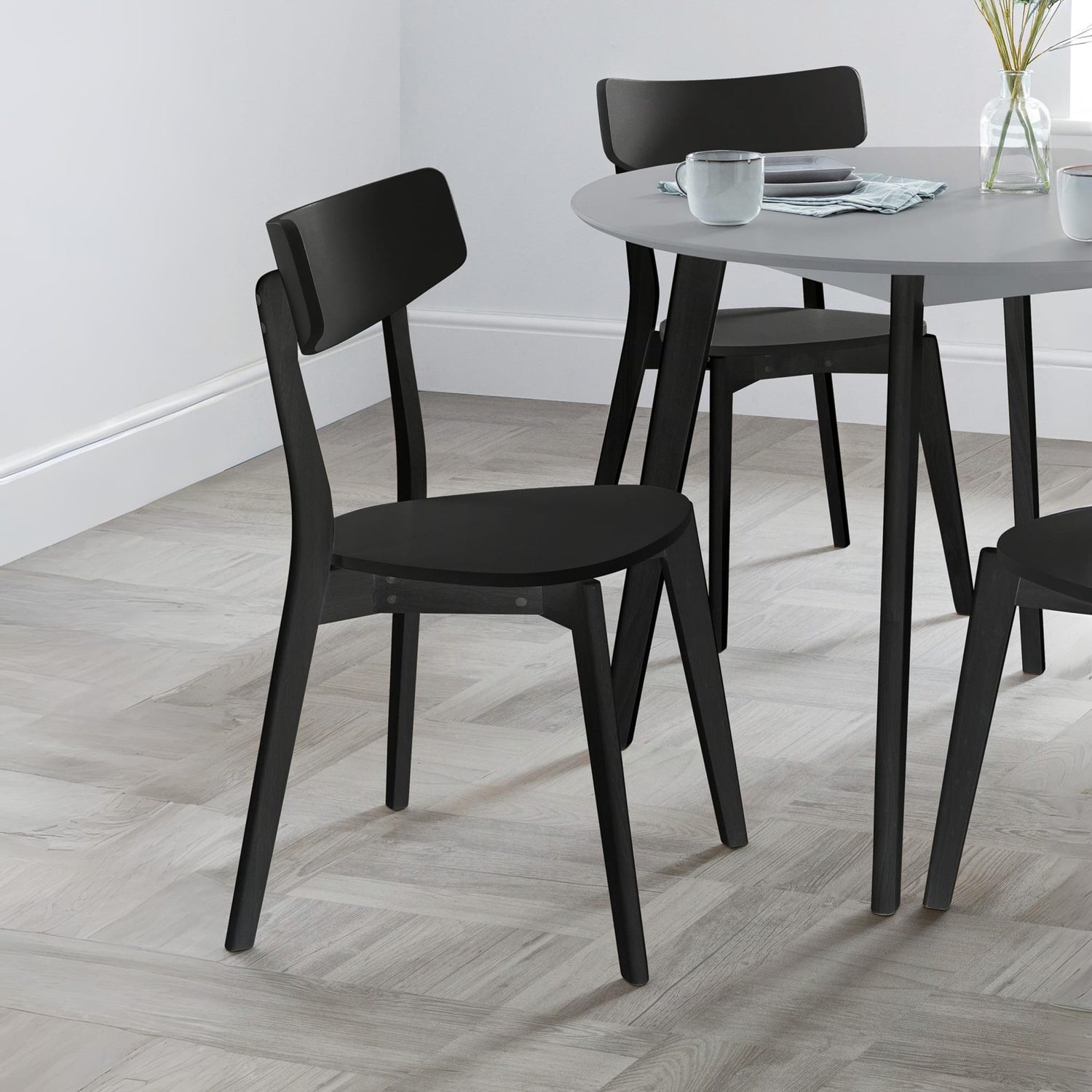 Black chairs around a round dining table with a white wall background
