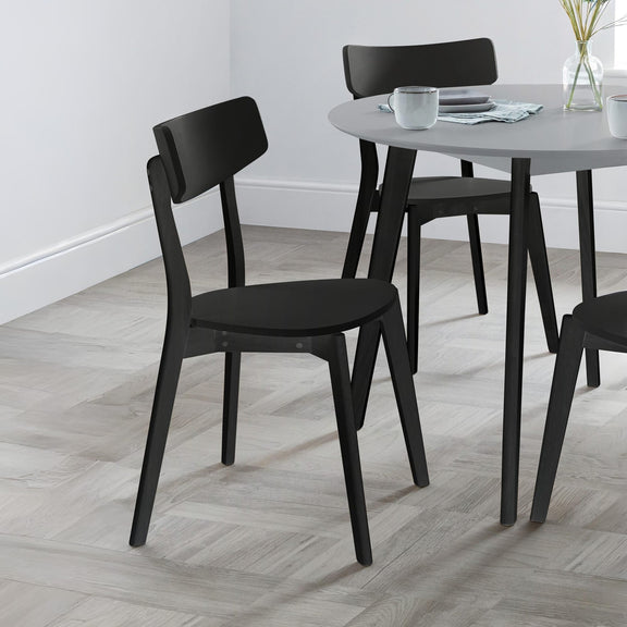 Black chairs around a round dining table with a white wall background