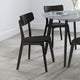 Black chairs around a round dining table with a white wall background