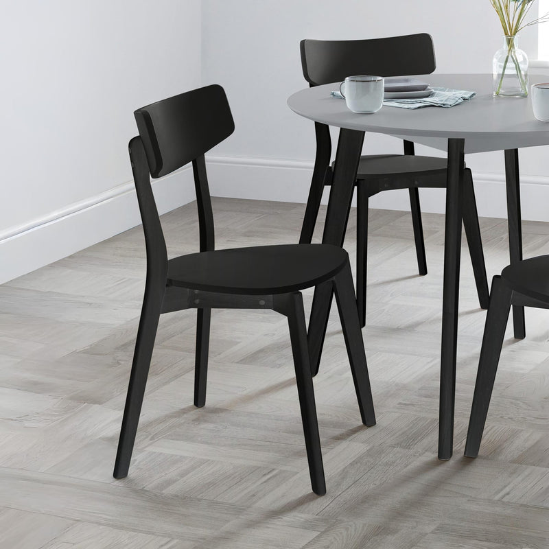 Black chairs around a round dining table with a white wall background