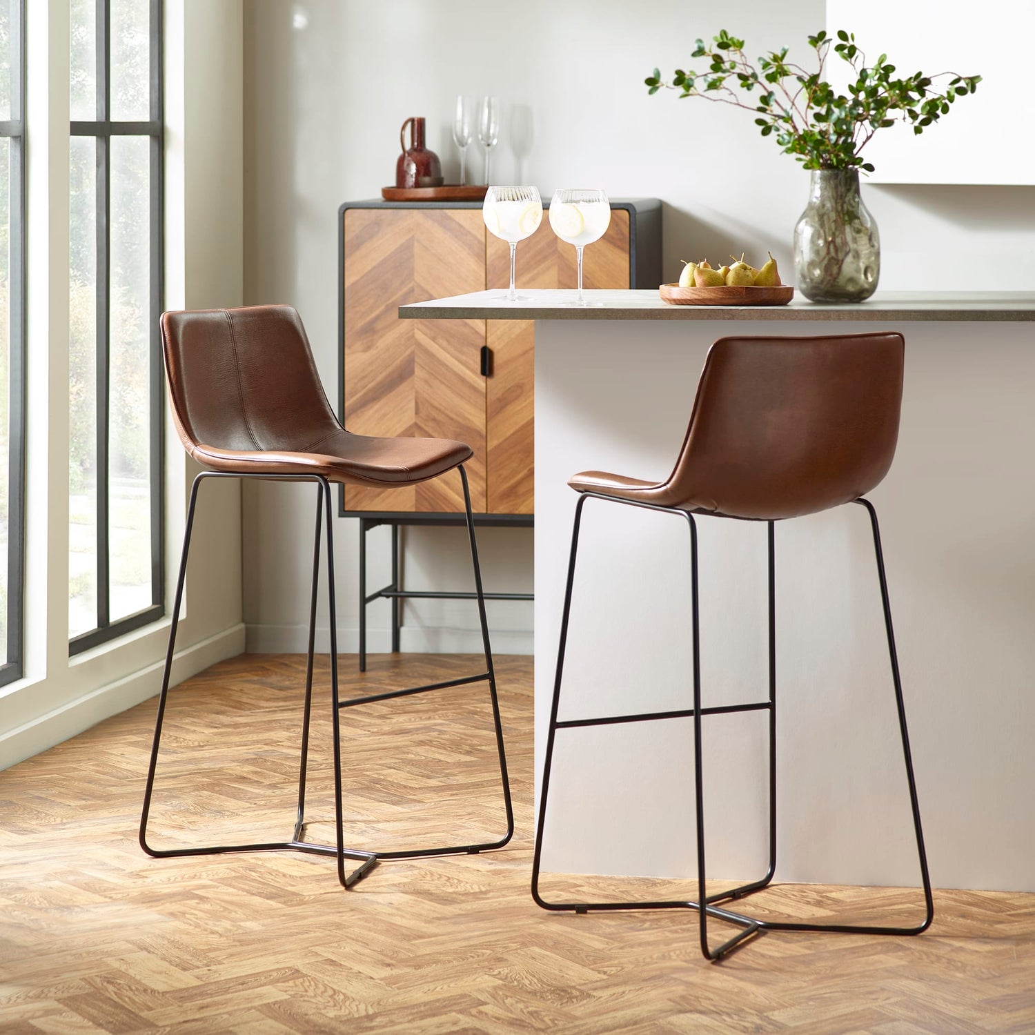 Two brown bar stools with black metal legs in a modern kitchen setting.