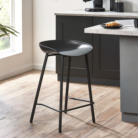 Black bar stool in a modern kitchen setting with gray cabinets and a window.