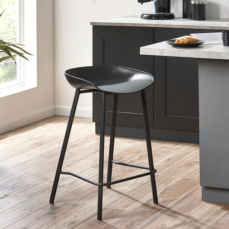 Black bar stool in a modern kitchen setting with gray cabinets and a window.