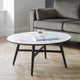 Round coffee table with a book and cup on it, placed in front of a gray sofa in a living room.