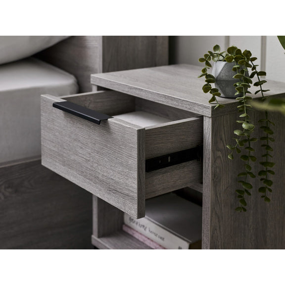 Wooden side table with open drawer, books, and a plant in a room setting.