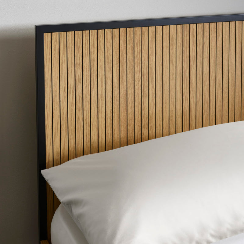 Wooden headboard with a pillow on a bed against a plain wall