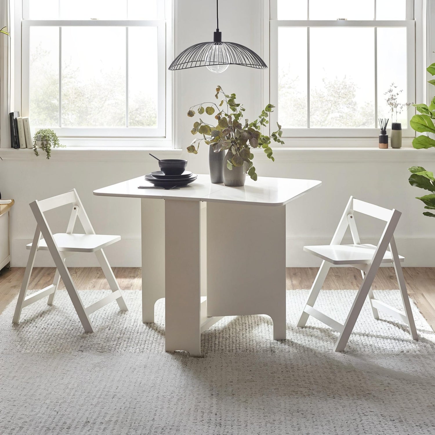 White dining table with chairs in a bright room with large windows.