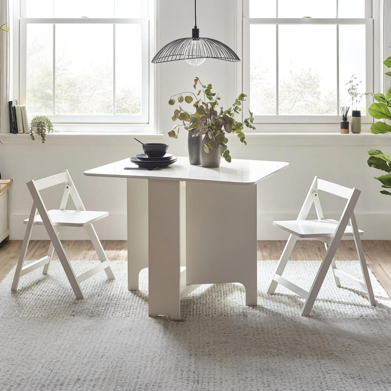 White dining table with chairs in a bright room with large windows.