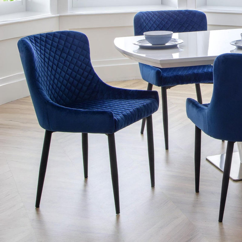 Blue velvet chairs around a round dining table in a bright room.