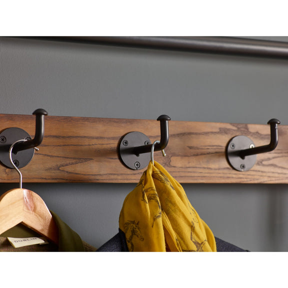 Wooden coat rack with black hooks holding a yellow scarf and green jacket against a gray background