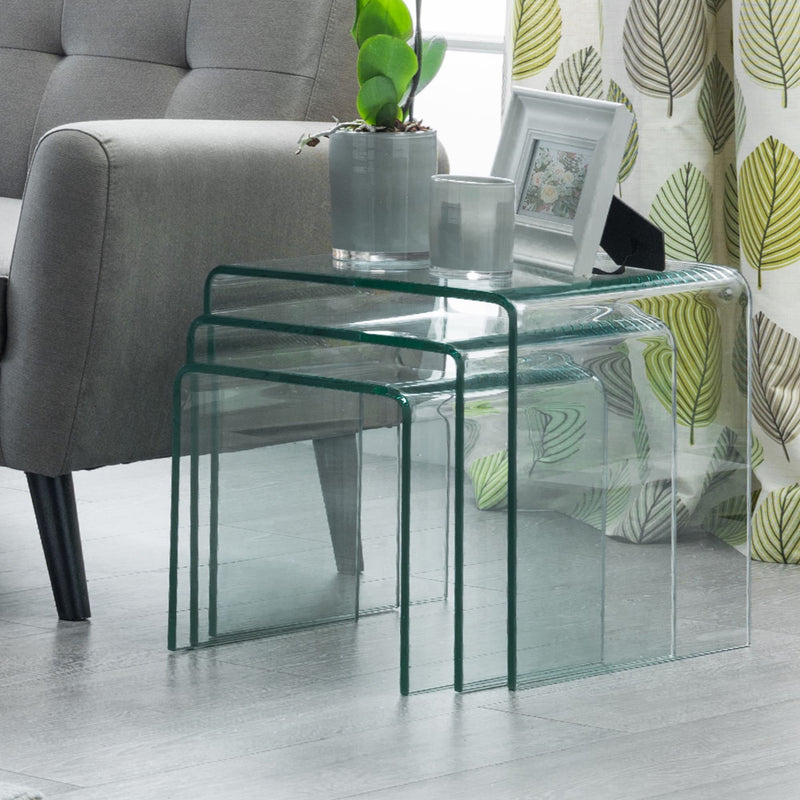 Glass nesting tables in a living room setting with a sofa and decorative elements.