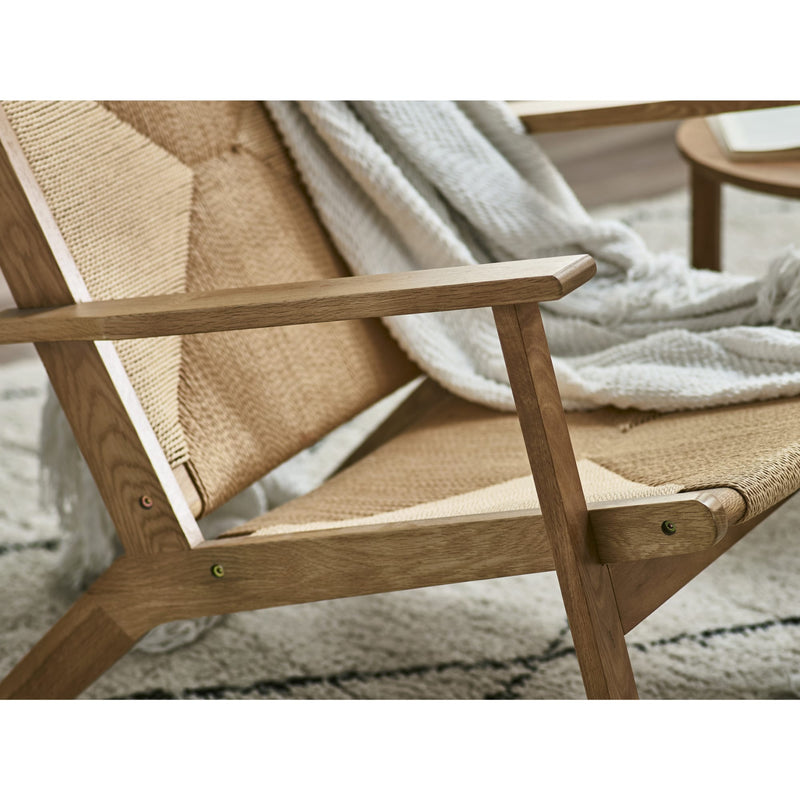 Wooden chair with woven backrest and armrests, draped with a white blanket on a neutral background.