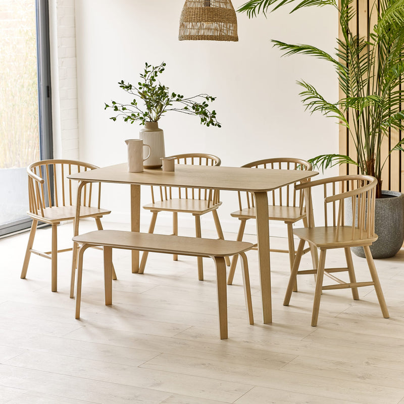 Dining set with table, chairs, and bench in a bright room with plants.