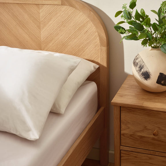 Wooden bed with white pillows and a nightstand with a plant