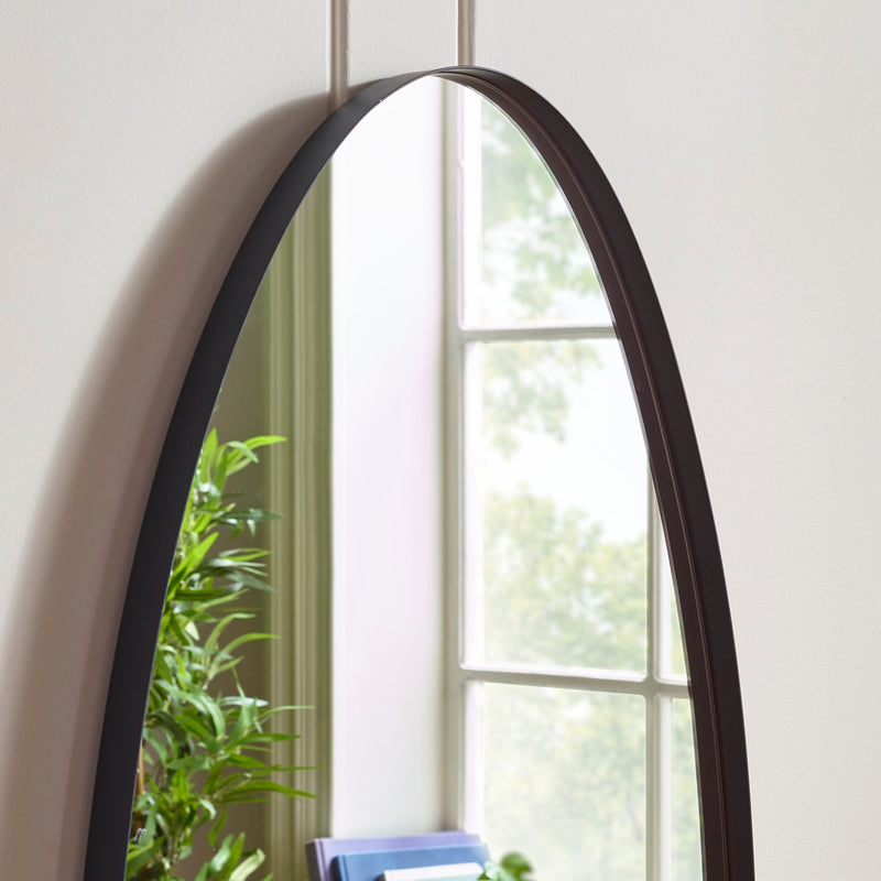 Arched mirror with black frame on a white wall with a window and plant in the background