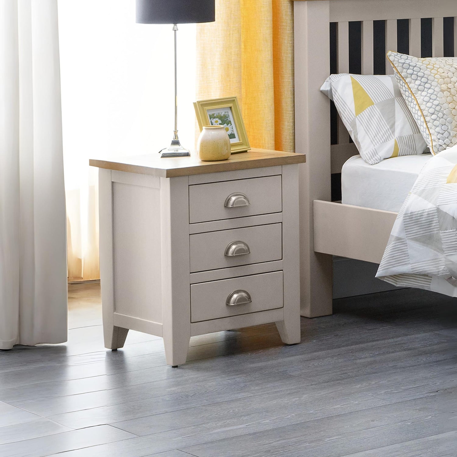 Beige nightstand with drawers next to a bed with white bedding and yellow accents.