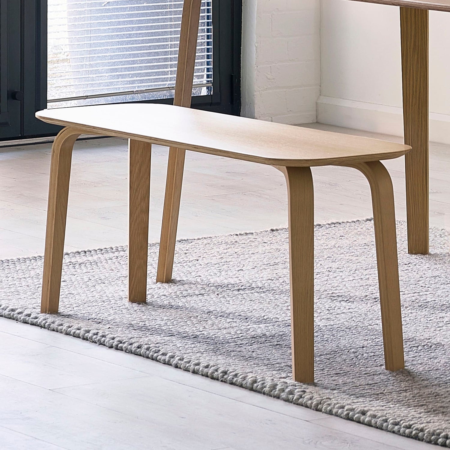 Wooden coffee table in a minimalistic room with a rug and window blinds.