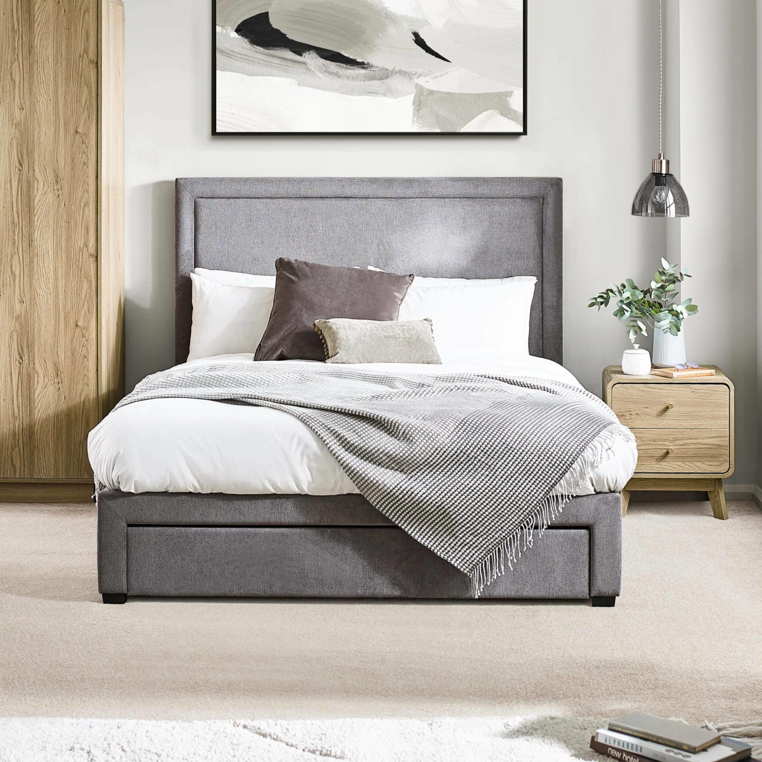 Gray upholstered bed in a bedroom setting with a side table and abstract art on the wall.