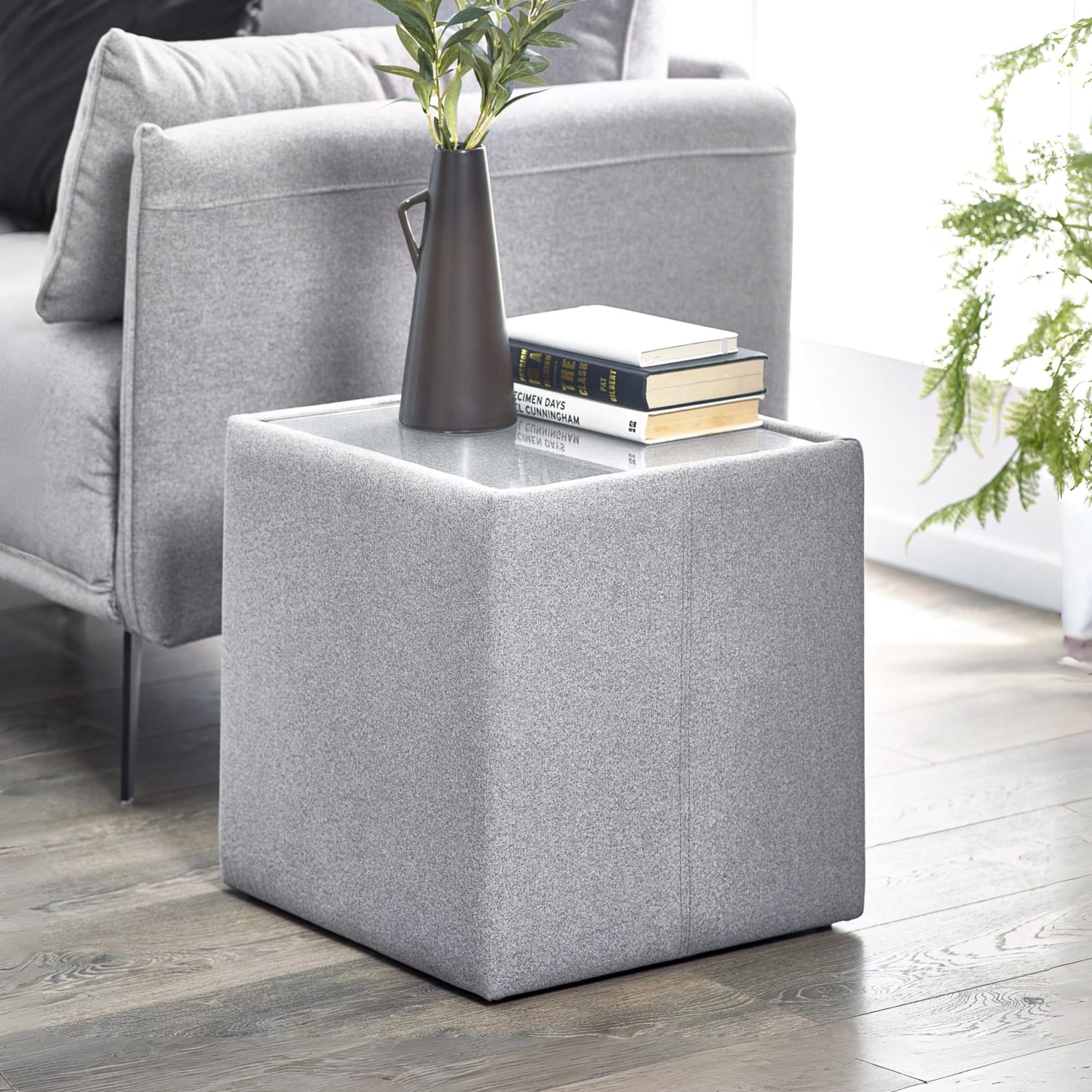 Gray upholstered side table with a vase and books next to a gray sofa.