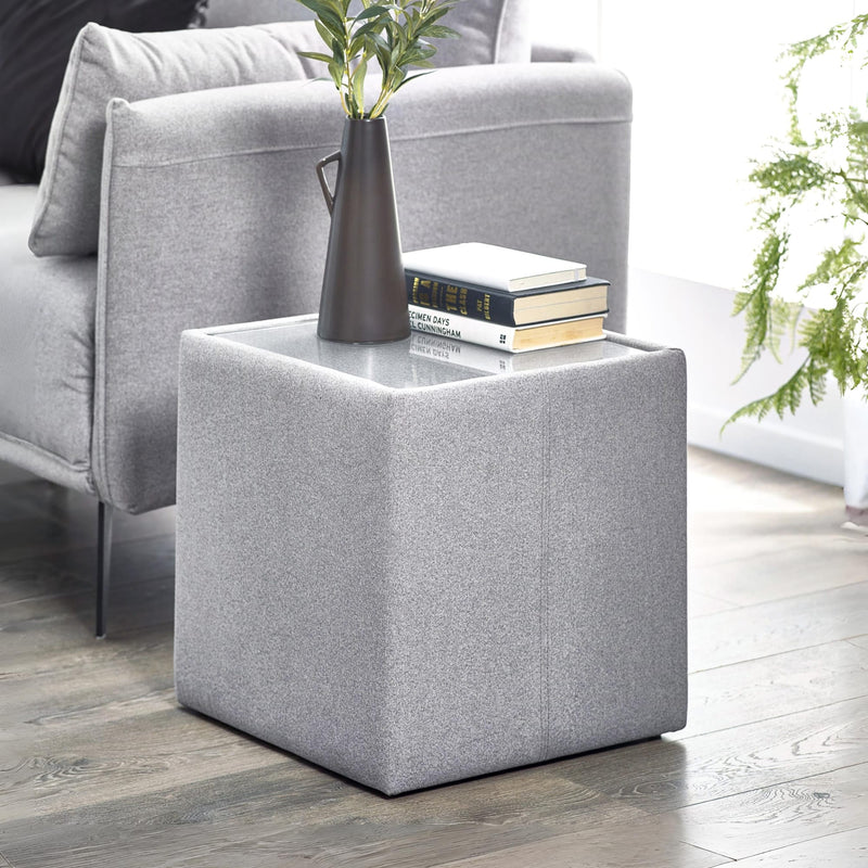 Gray upholstered side table with a vase and books next to a gray sofa.
