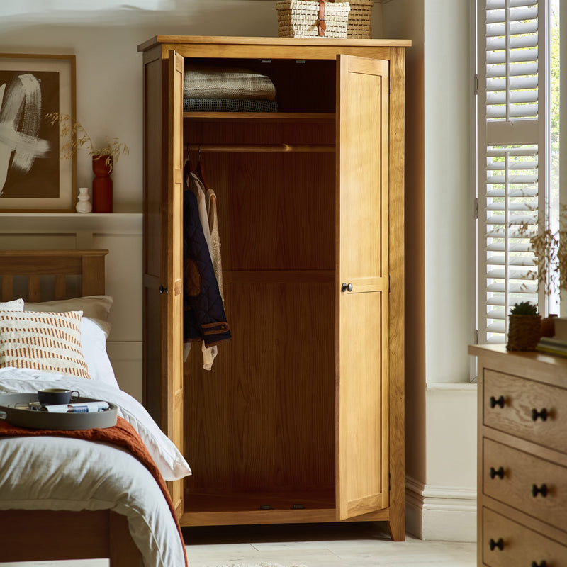 Wooden wardrobe in a bedroom with open doors, showing clothes inside.