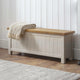 Wooden bench with a blanket draped over it against a white paneled wall.