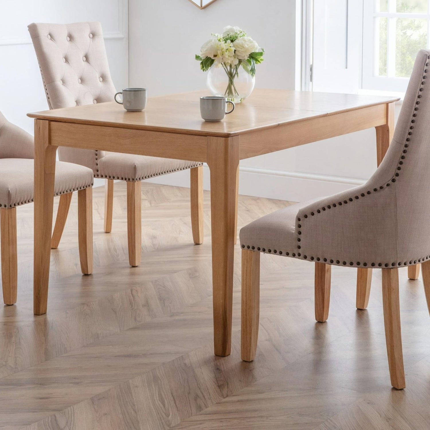 Dining table with chairs and a vase of flowers in a bright room.