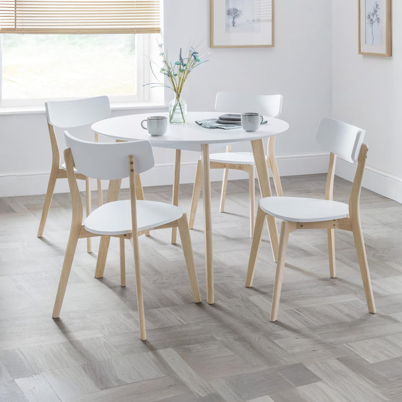 Round white dining table with four matching chairs in a bright room.