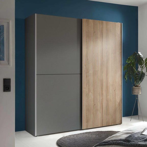 Modern wardrobe with gray and wooden doors in a room with blue walls and a plant.