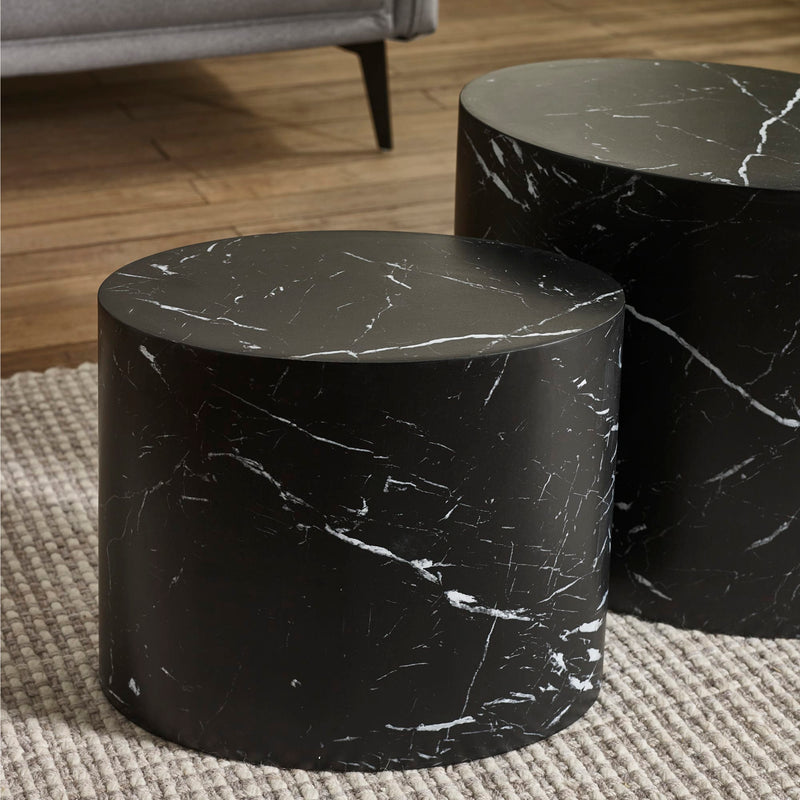 Two black marble cylindrical tables on a textured rug with a blurred background.