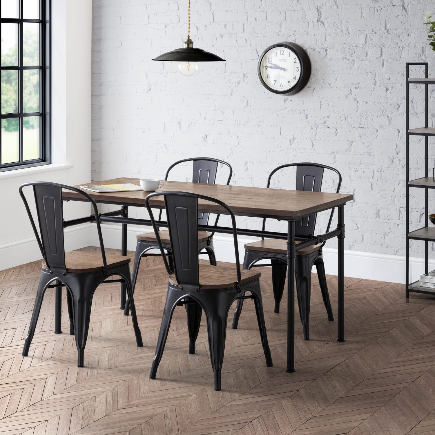 Dining area with wooden table and black metal chairs against a white brick wall.
