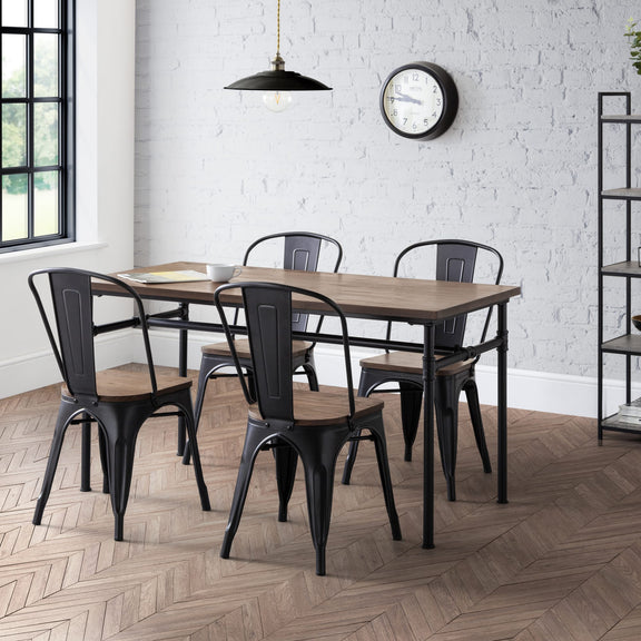 Dining area with wooden table and black metal chairs against a white brick wall.